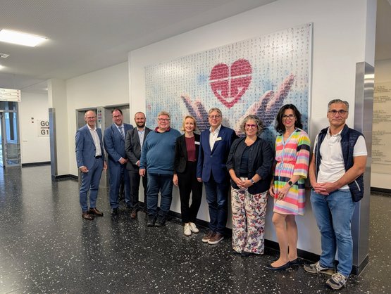 Neun Personen posieren vor einem Herzbild im Krankenhausflur.