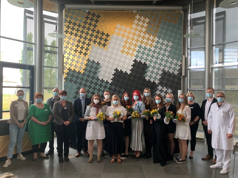 Gruppe von Menschen mit Masken, hält Blumensträuße vor bunter Wand.