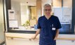 Chefarzt in blauer Uniform vor der Rezeption der Klinik in München.