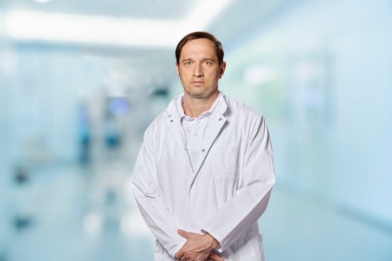 Arzt im weißen Kittel steht in einem modernen Krankenhausflur.