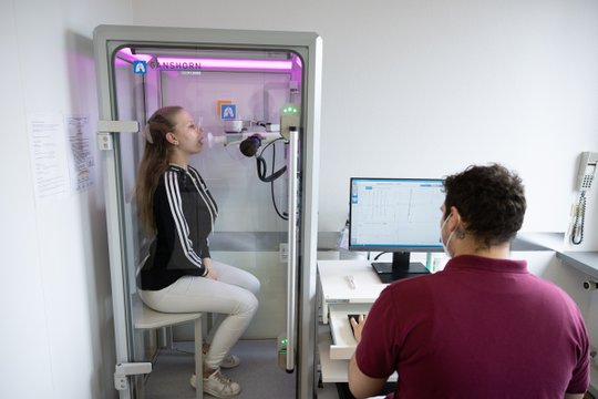 Patientin bei Ganzkörper-Plethysmographie, Arzt überwacht die Lungenfunktionsmessung.