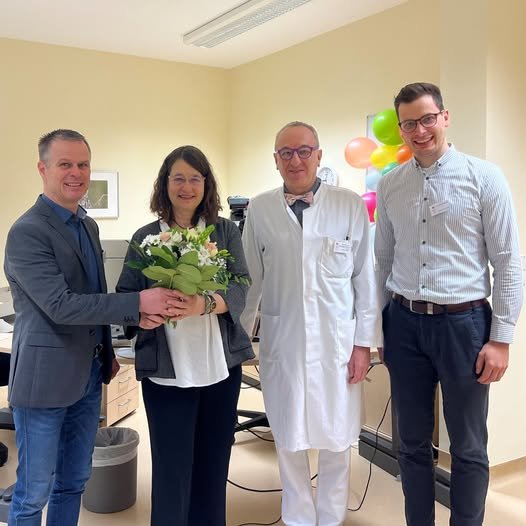 Vier Personen, eine Frau mit Blumenstrauß, stehen lächelnd in einem Büro.