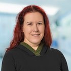 Porträt einer lächelnden Frau mit rotem Haar und schwarzem Oberteil.