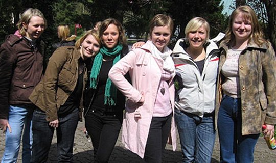 Sechs junge Frauen lächeln in die Kamera bei einem Seminar im Freien.