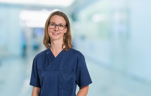 Ärztin in blauer Arbeitskleidung lächelt in einem Krankenhausflur.