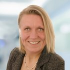 Porträt einer lächelnden Frau mit blondem Haar und Perlenkette.