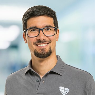 Mann mit Brille und Bart lächelt vor unscharfem Hintergrund im Büro.
